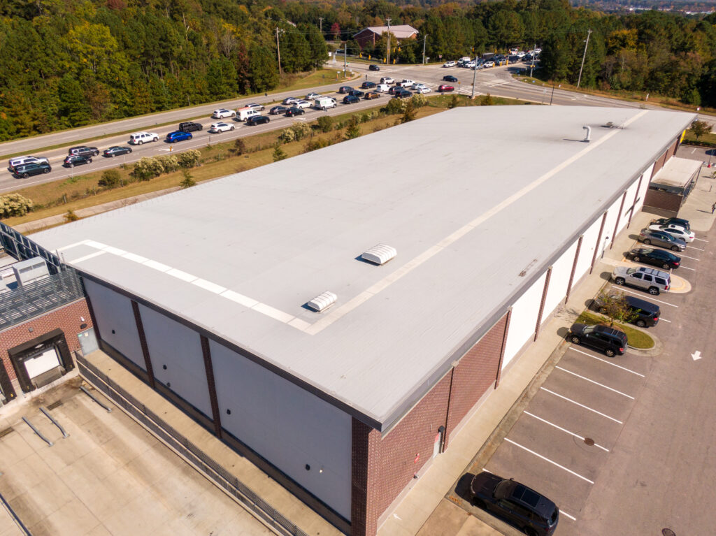 Aerial view of a commercial building roof and surrounding parking area.