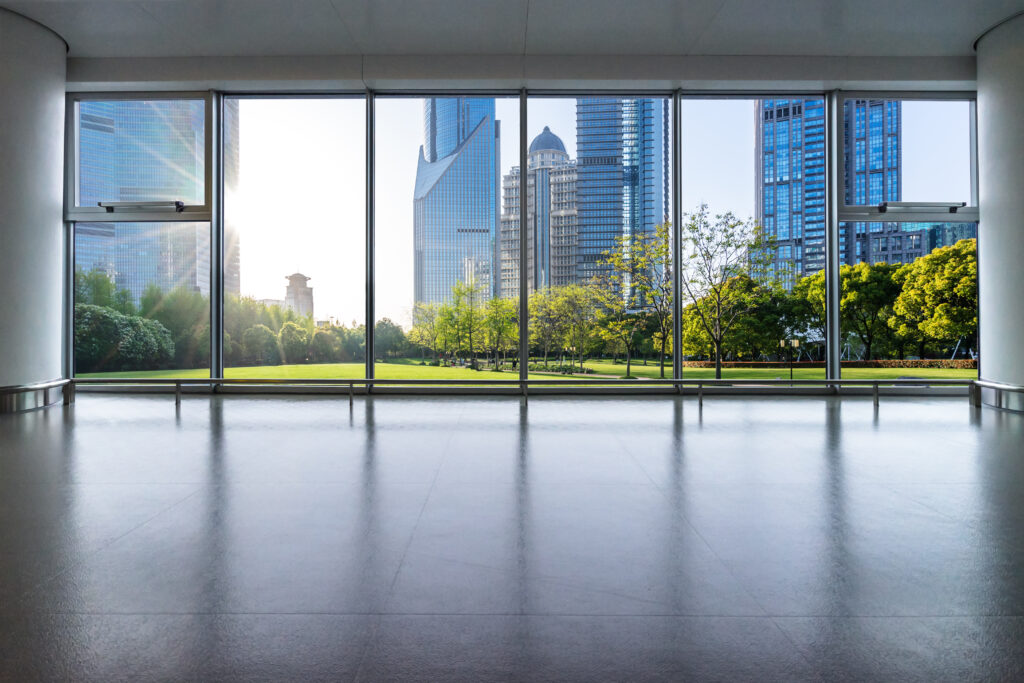 Empty office interior with floor-to-ceiling windows overlooking landscaped commercial buildings.