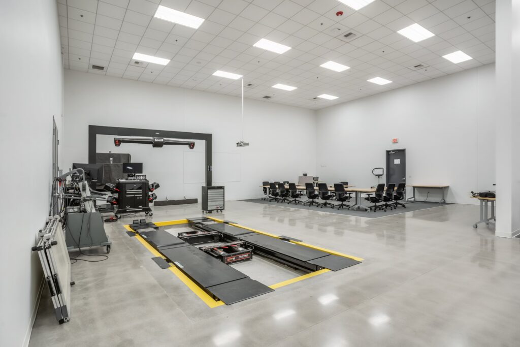 Automotive training bay with a floor-mounted vehicle lift, equipment and classroom tables.