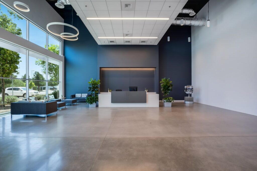 Reception lobby with a front desk, tall windows, ring lights and polished concrete flooring.