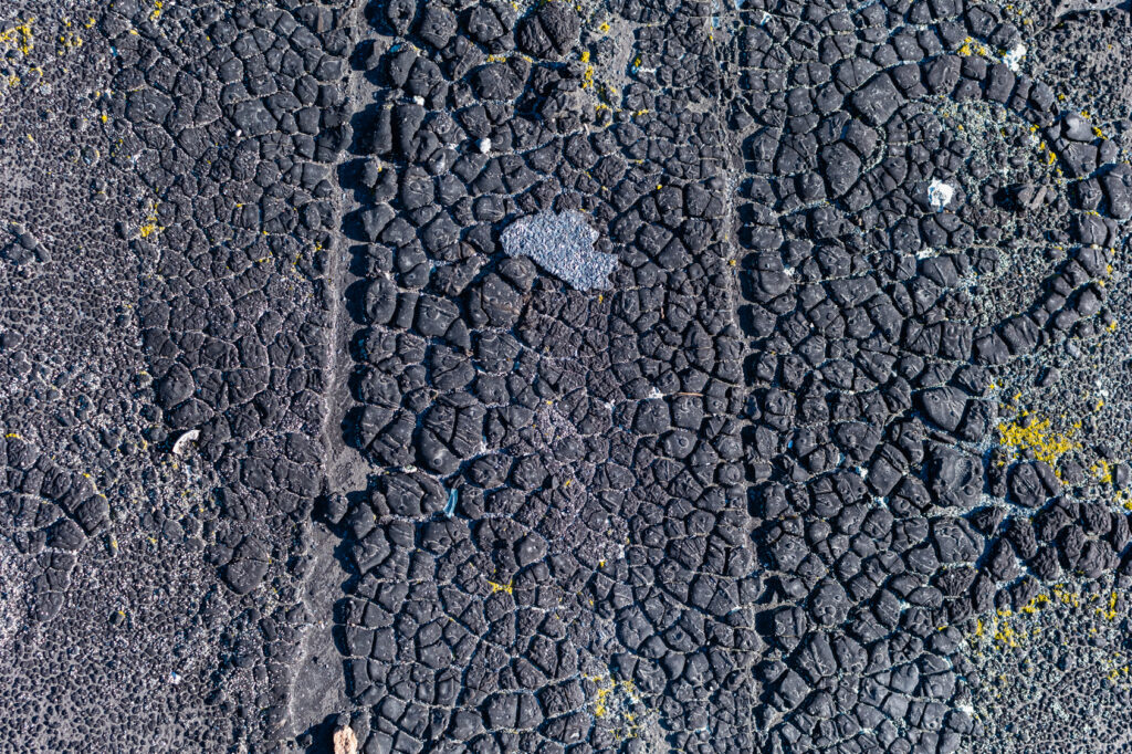Close view of cracks and weathering in a black roof-surface coating.