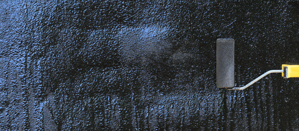 Roller applying dark coating across a textured roof surface.