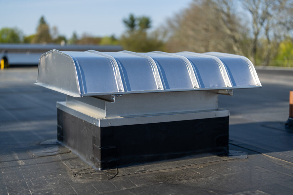 Metal exhaust vent on a raised curb above a black commercial roofing membrane.