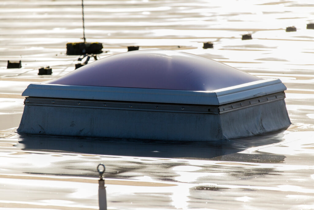 Domed skylight and raised curb surrounded by water on a low-slope roof.