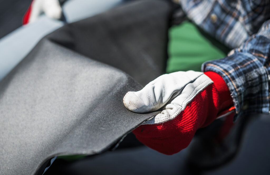 Gloved hand holding a folded sheet of dark roofing membrane.
