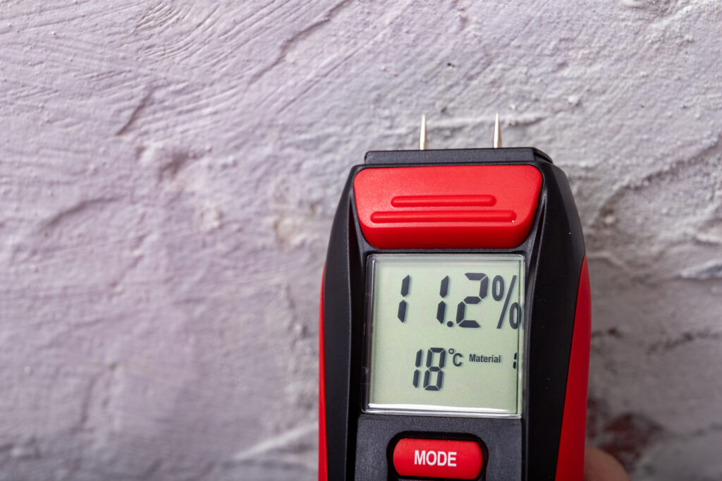 Digital moisture meter held against a plaster wall