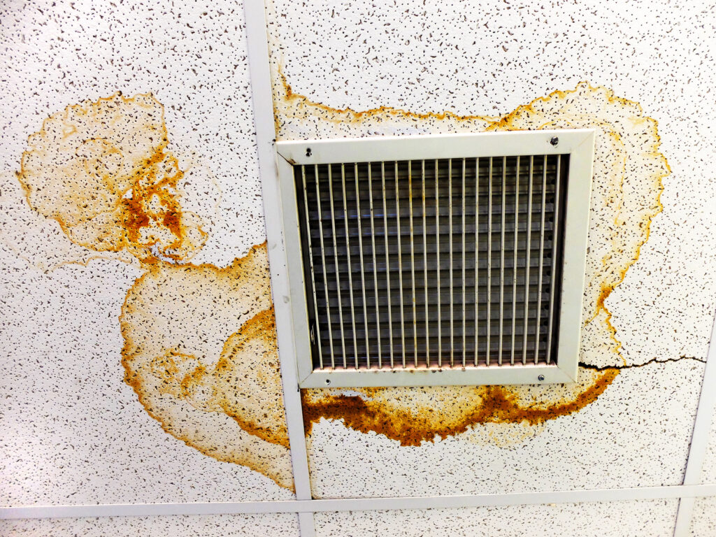 Water-stained suspended ceiling tiles surrounding an air vent